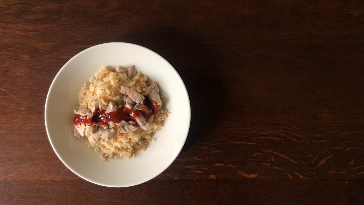 A bowl of chicken rice, topped with chicken and chilli sauce