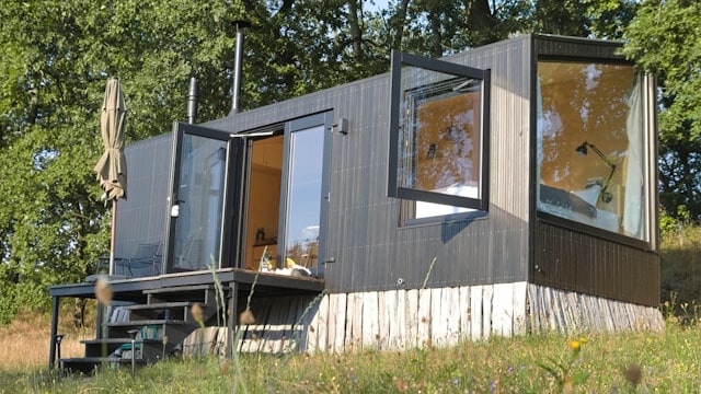 A container-shaped tiny house on a grassy slope with trees in the background